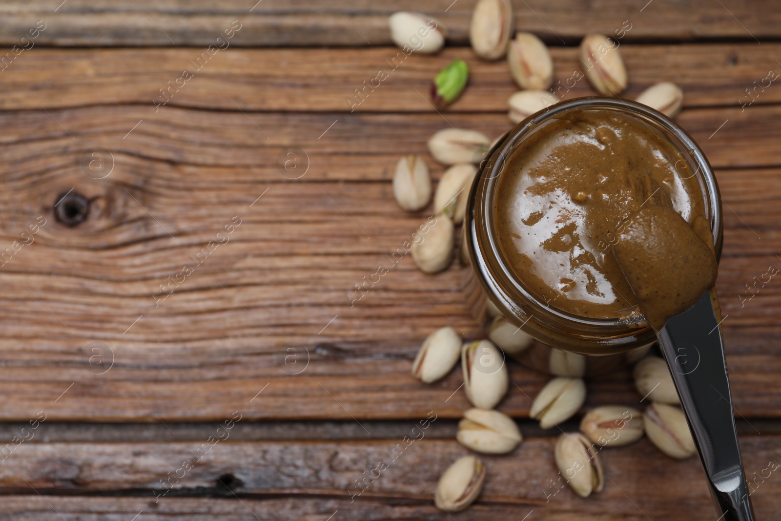 Photo of Tasty pistachio nut paste and knife on wooden table, flat lay. Space for text