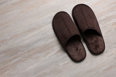 Photo of Pair of brown slippers on white wooden floor, top view. Space for text