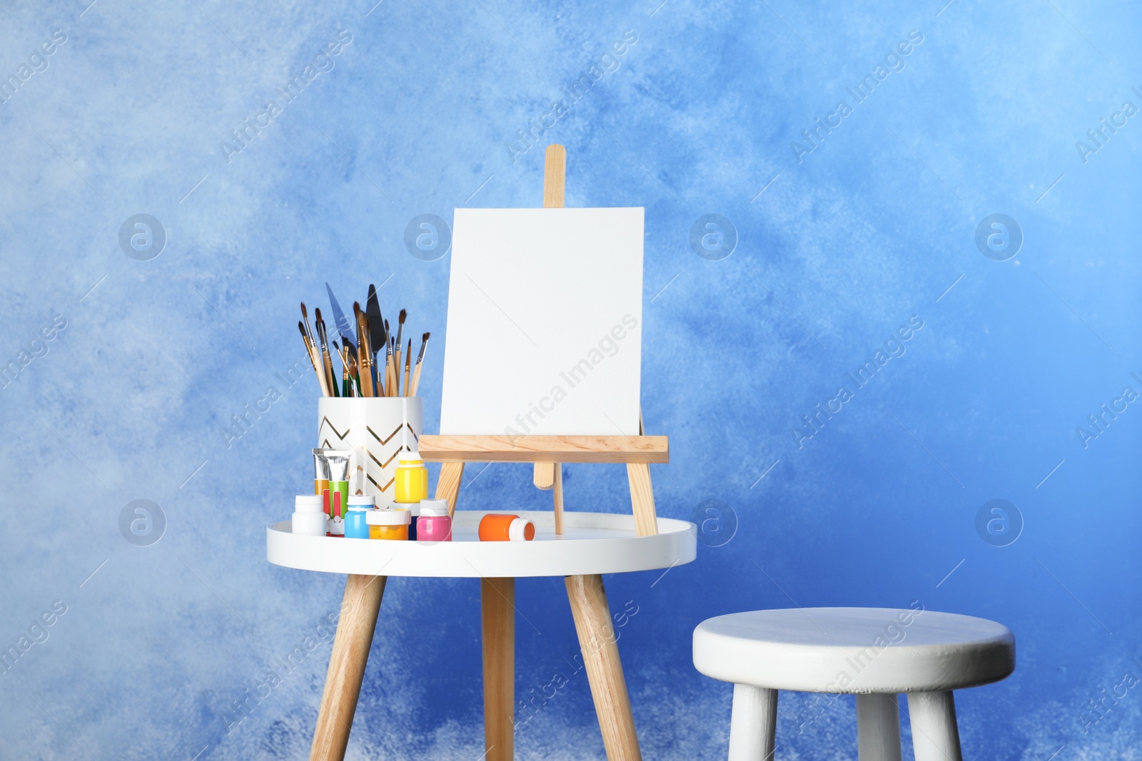 Photo of Wooden easel with blank canvas board and painting tools for children on table near color wall