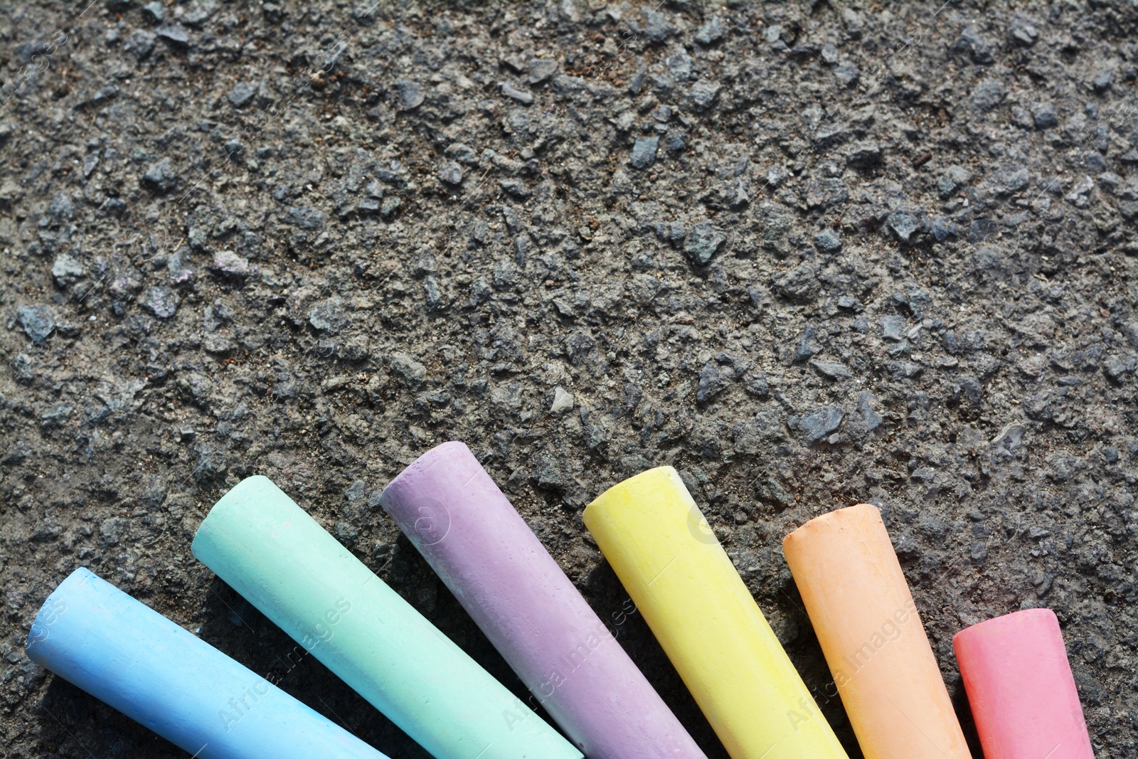 Photo of Colorful chalk sticks on asphalt, flat lay. Space for text