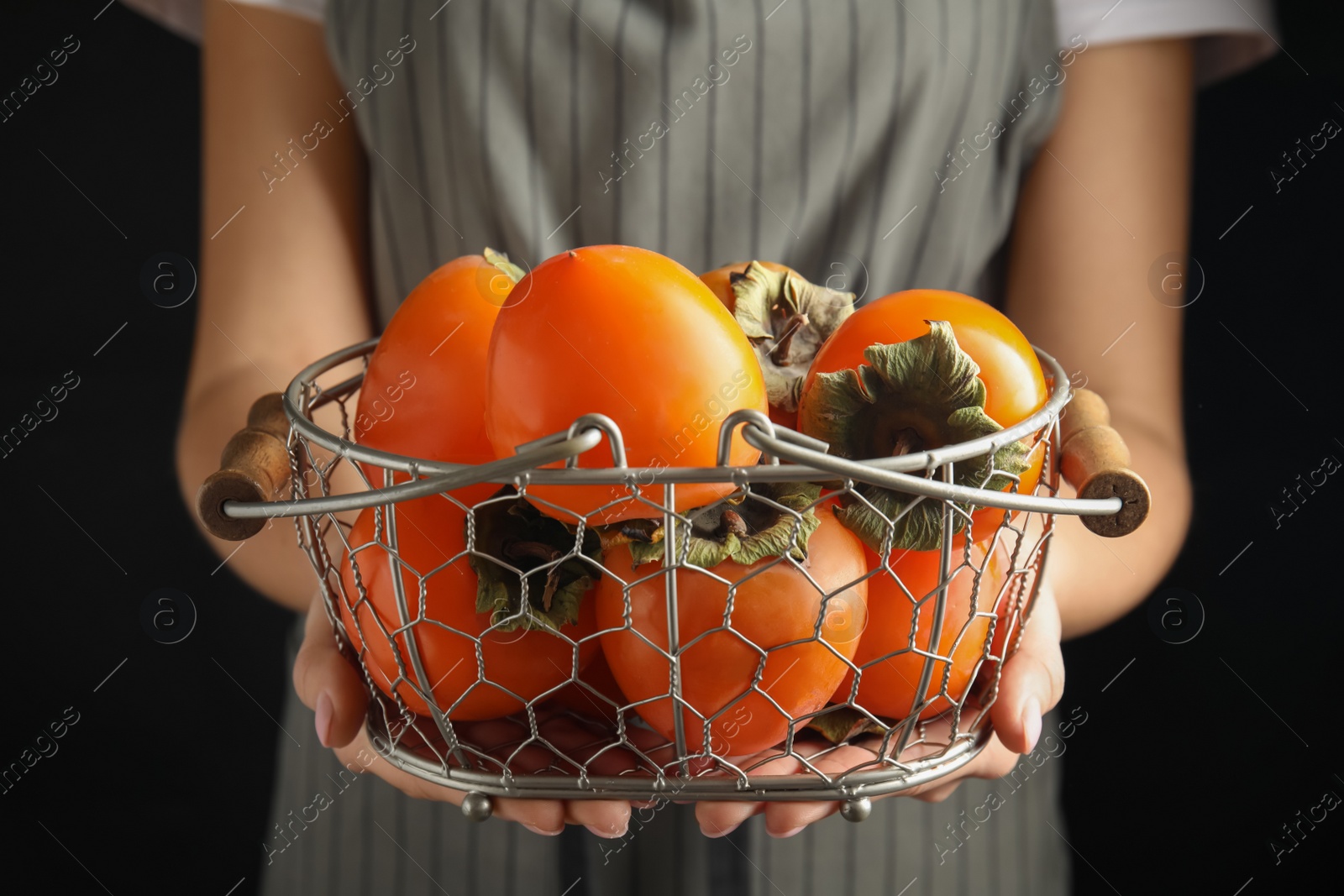 Photo of Woman holding delicious fresh persimmons on black background, closeup