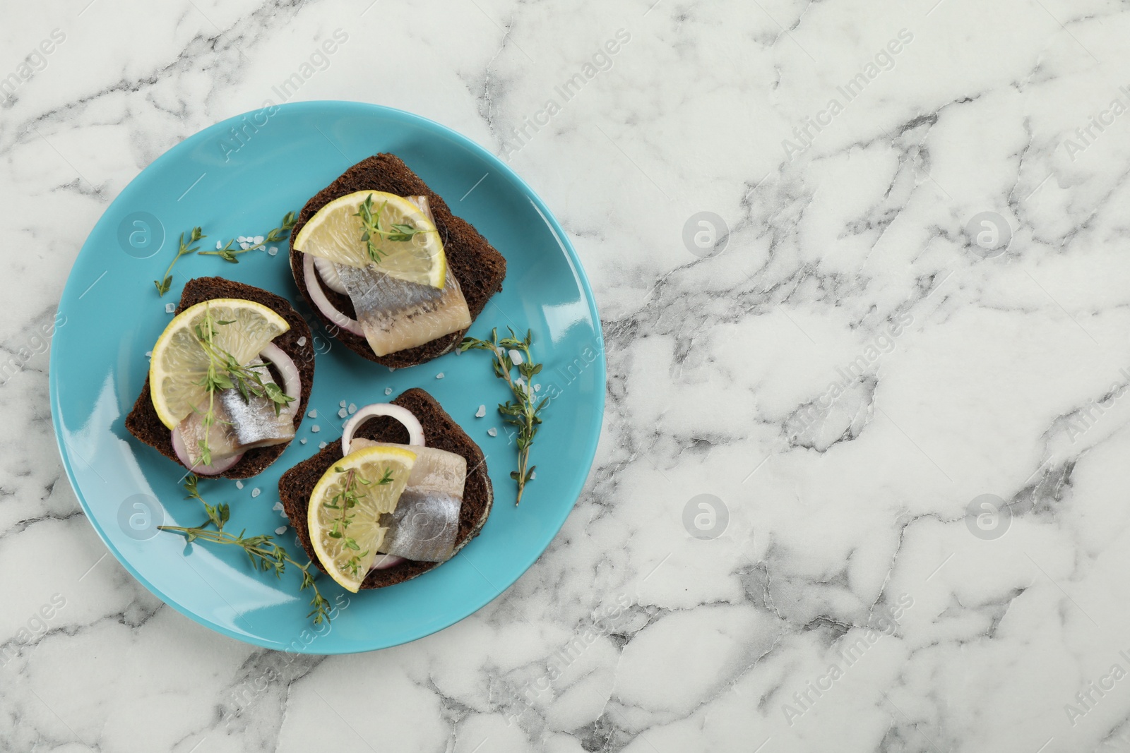 Photo of Delicious sandwiches with salted herring, onion rings and lemon on white marble table, top view. Space for text