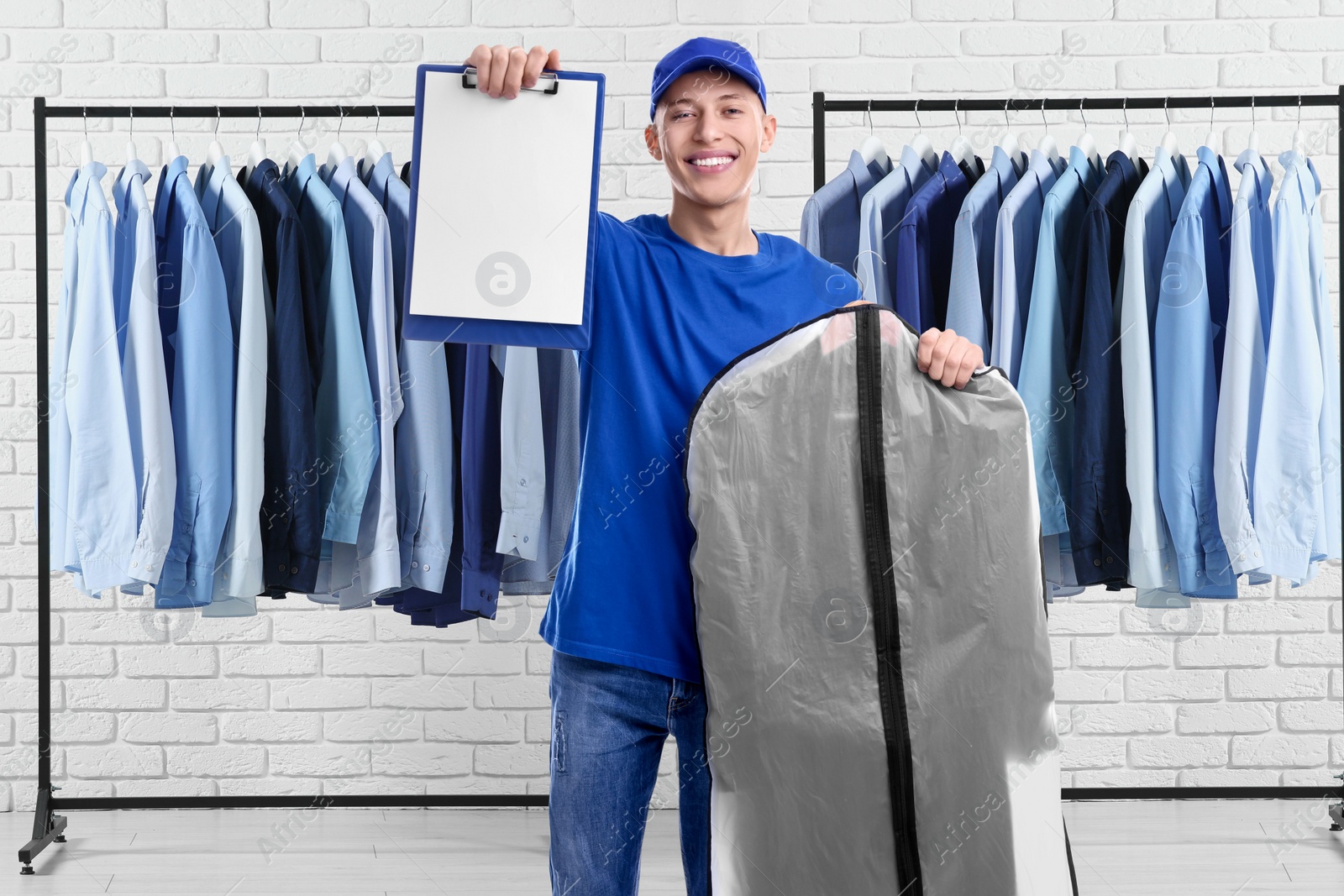 Image of Happy courier with garment cover of clothes showing clipboard in dry-cleaning