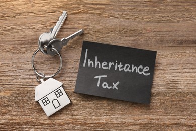 Photo of Inheritance Tax. Card and keys with key chain in shape of house on wooden table, top view