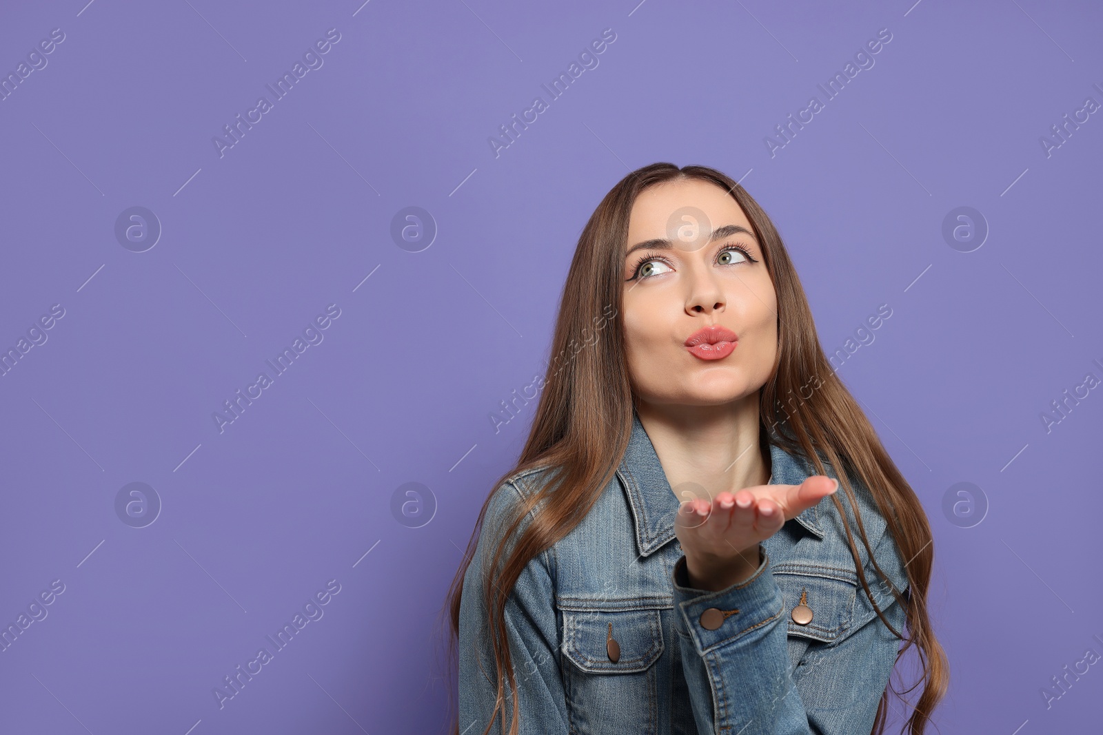 Photo of Beautiful young woman blowing kiss on purple background, space for text