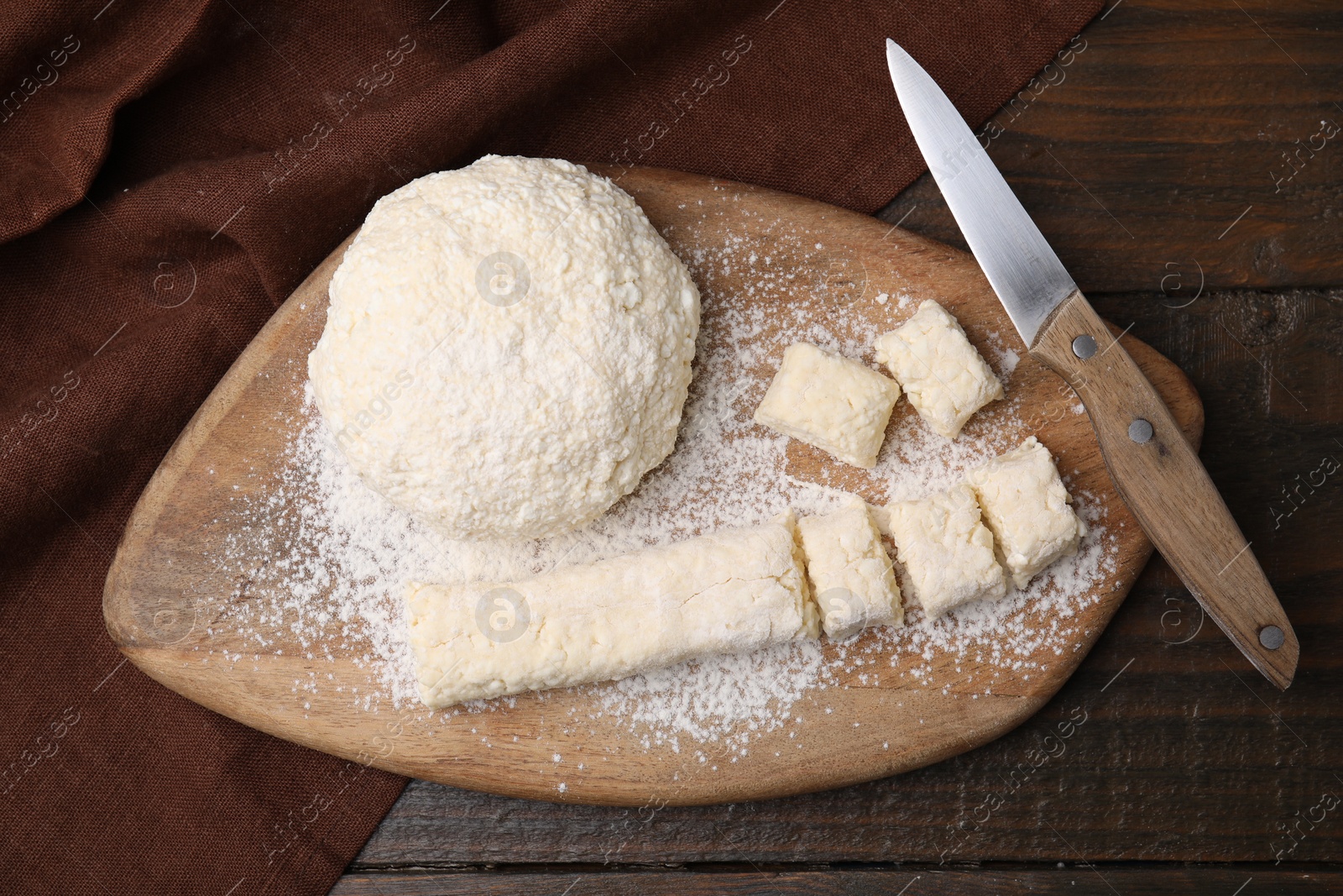 Photo of Making lazy dumplings. Board with raw dough, flour and knife on wooden table, flat lay