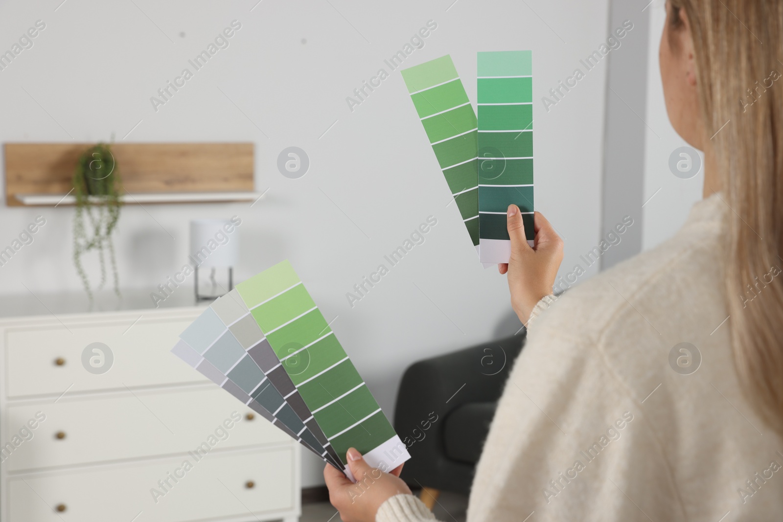 Photo of Woman choosing color for wall in room, focus on hands with paint chips. Interior design