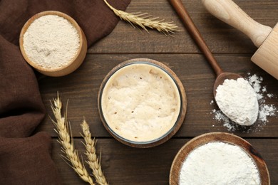 Photo of Leaven, flour, rolling pin and ears of wheat on wooden table, flat lay