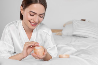 Photo of Happy woman taking hand cream from jar in bedroom