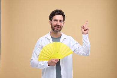 Happy man holding hand fan on beige background