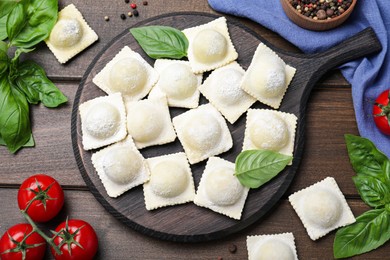 Photo of Uncooked ravioli, basil and tomato on wooden table, flat lay