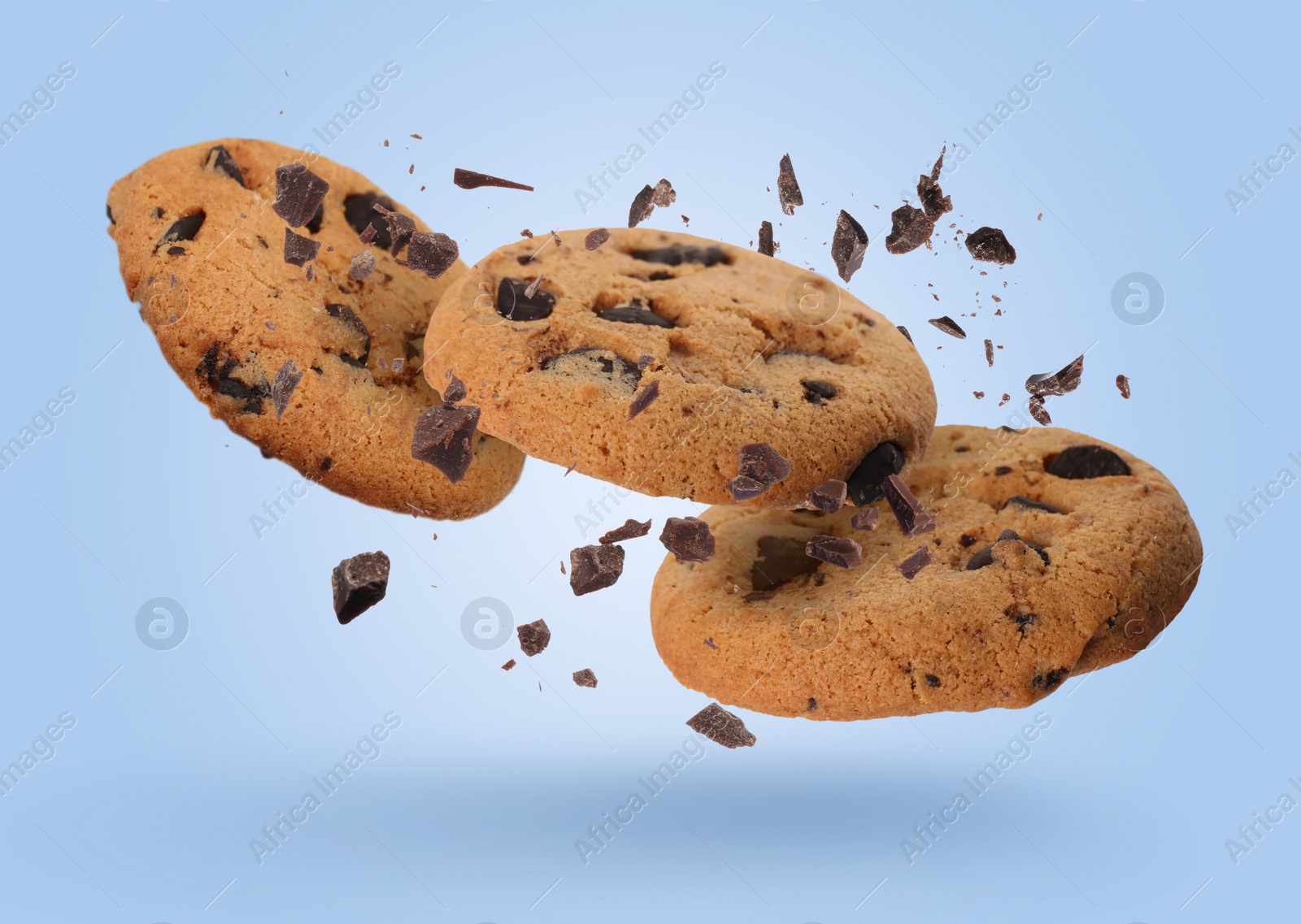 Image of Tasty chocolate chip cookies falling on light blue background