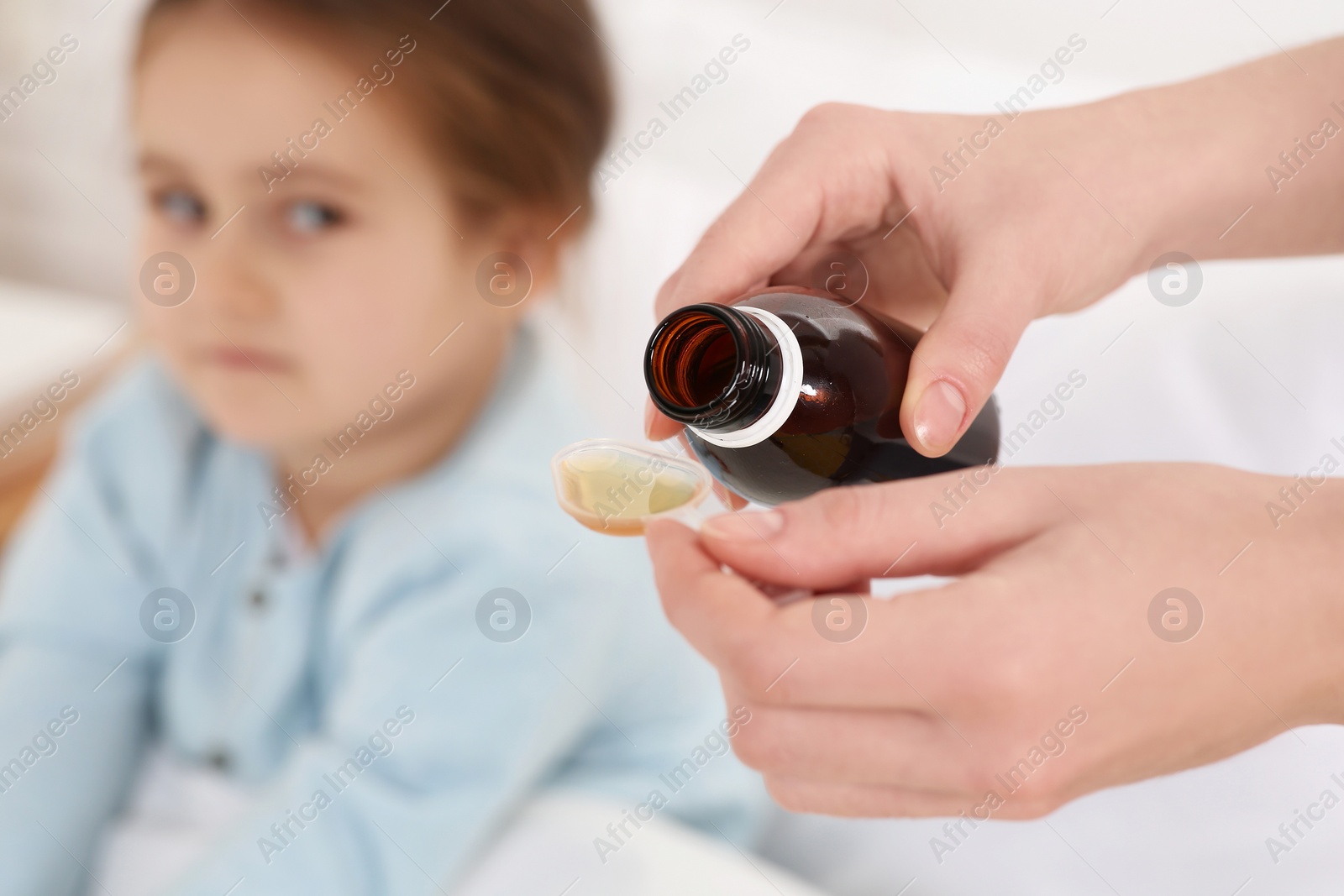 Photo of Mother pouring cough syrup into measuring spoon for her daughter indoors, focus on hands