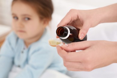Photo of Mother pouring cough syrup into measuring spoon for her daughter indoors, focus on hands