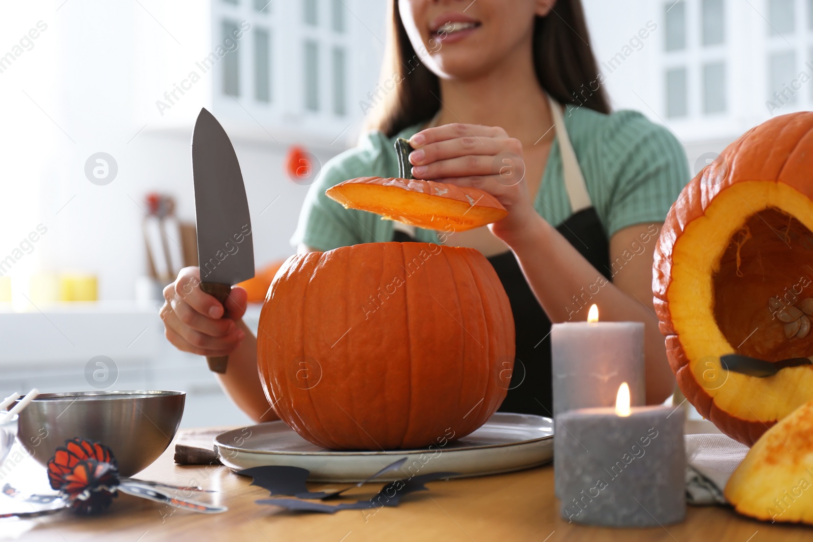 Photo of Woman making pumpkin jack o'lantern at table in kitchen, closeup. Halloween celebration