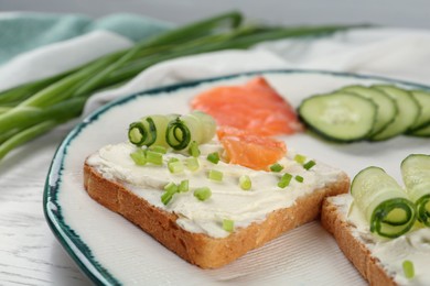 Toasted bread with cream cheese, salmon and cucumber on plate, closeup