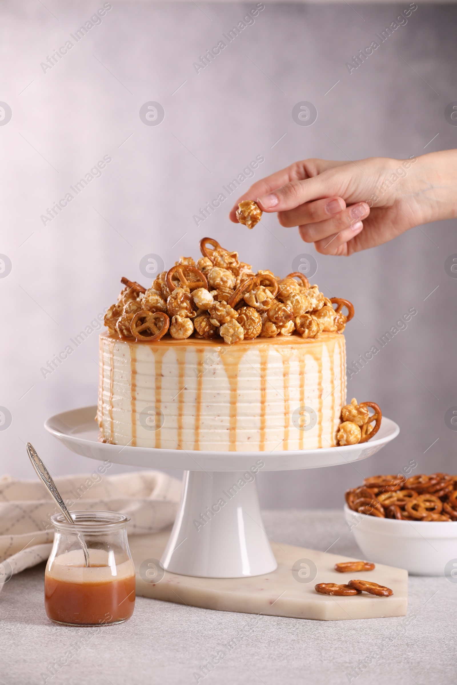 Photo of Woman decorating caramel drip cake at light table, closeup