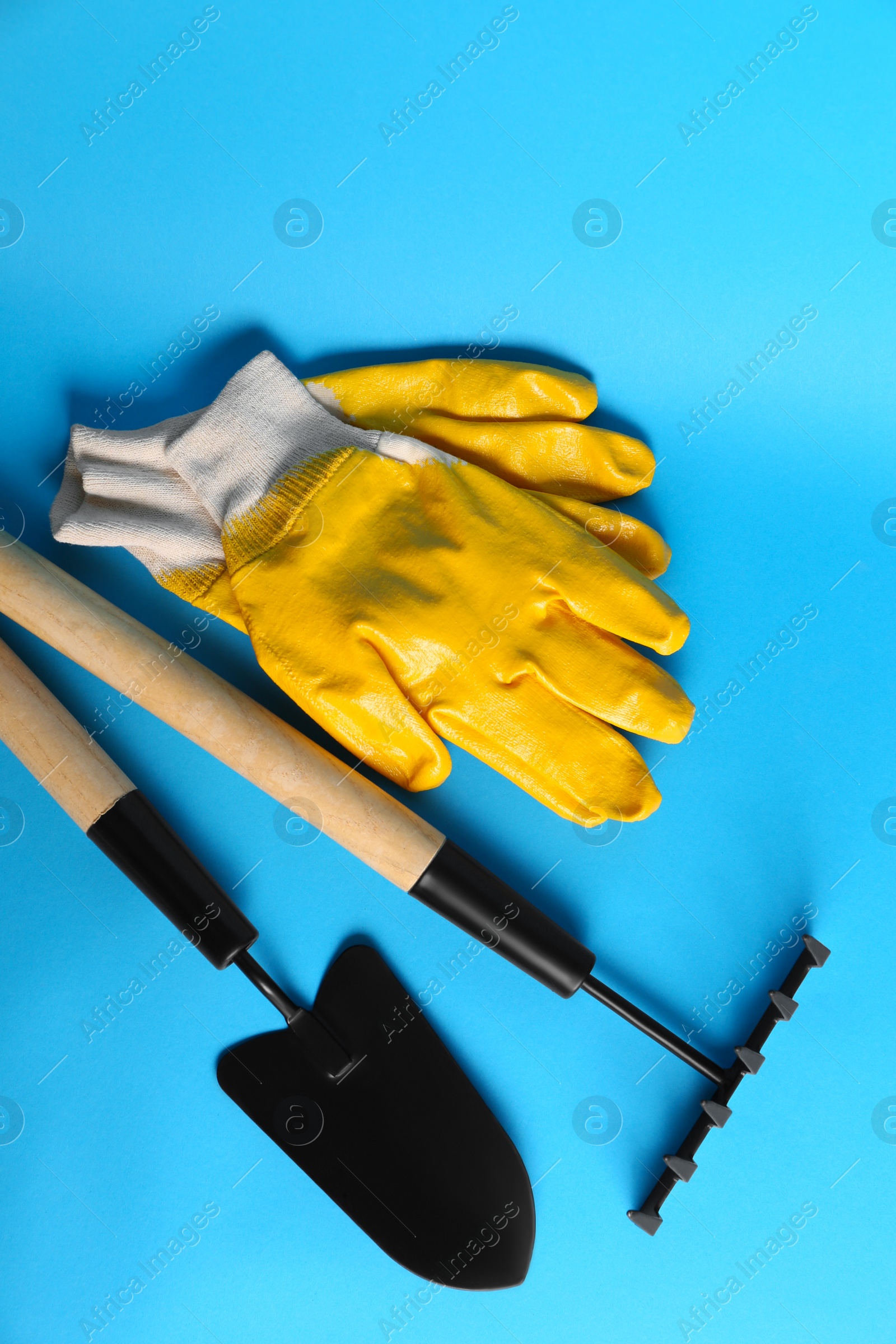 Photo of Gardening gloves, trowel and rake on light blue background, flat lay