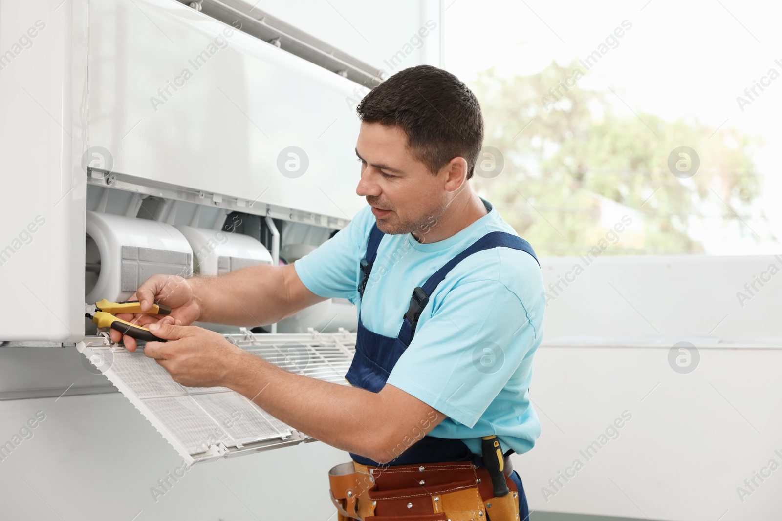 Photo of Male technician repairing modern air conditioner indoors