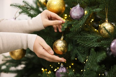 Photo of Woman decorating fir tree with golden Christmas ball indoors, closeup