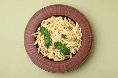 Photo of Plate of delicious trofie pasta with cheese and basil leaves on light olive background, top view