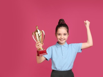 Photo of Happy girl in school uniform with golden winning cup on pink background. Space for text