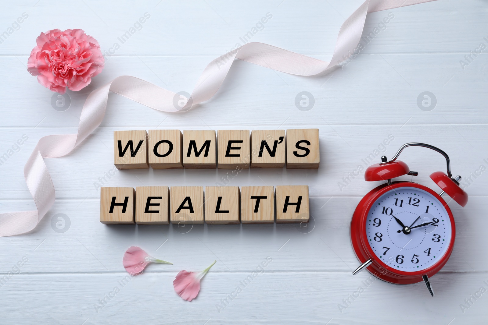 Photo of Wooden cubes with words Women's Health, alarm clock, ribbon and pink carnation flower on white table, flat lay