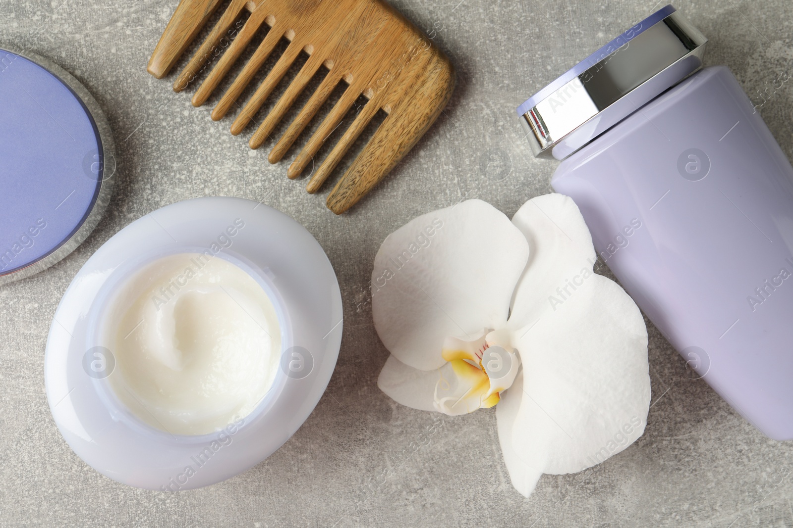 Photo of Hair care cosmetic products, orchid flower and comb on grey table, flat lay