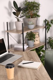 Beautiful workplace with laptop on wooden table and houseplants in room