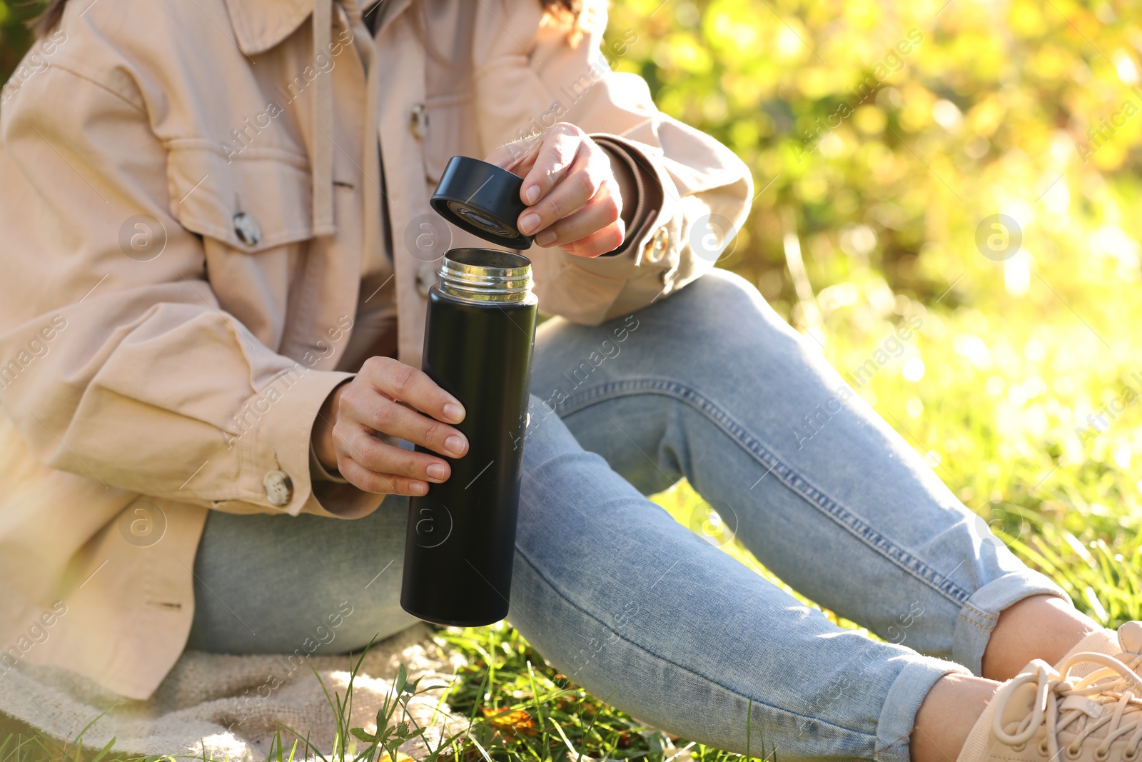 Photo of Woman opening thermos on green grass outdoors, closeup