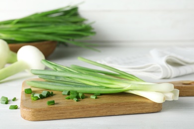 Photo of Wooden board with cut fresh green onions on white table