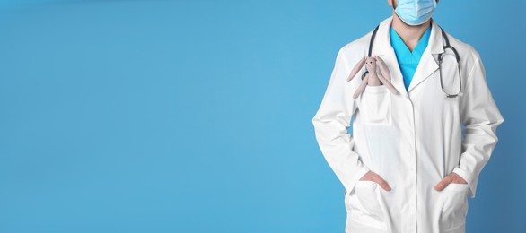 Photo of Pediatrician with toy bunny and stethoscope on light blue background, closeup. Space for text