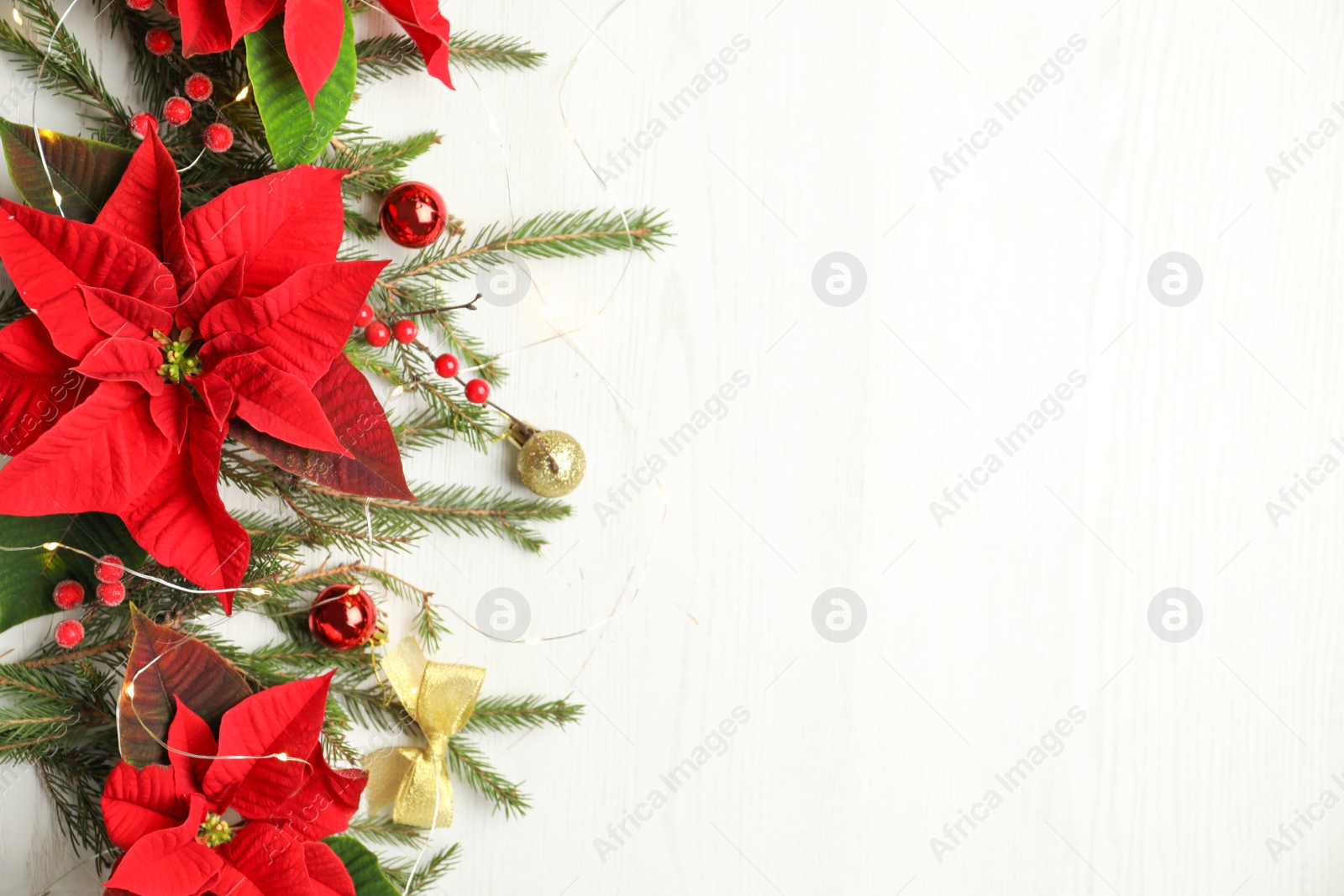 Photo of Flat lay composition with poinsettias (traditional Christmas flowers) and holiday decor on white wooden table. Space for text