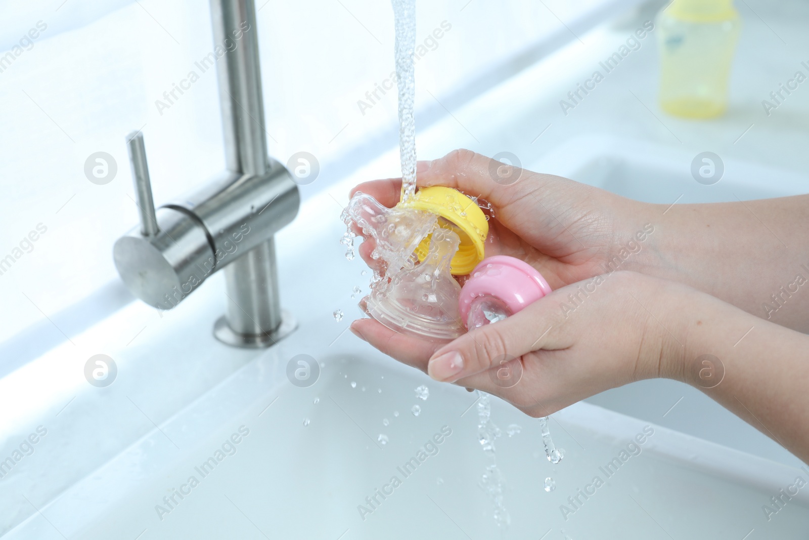 Photo of Woman washing baby bottle nipples under stream of water, closeup