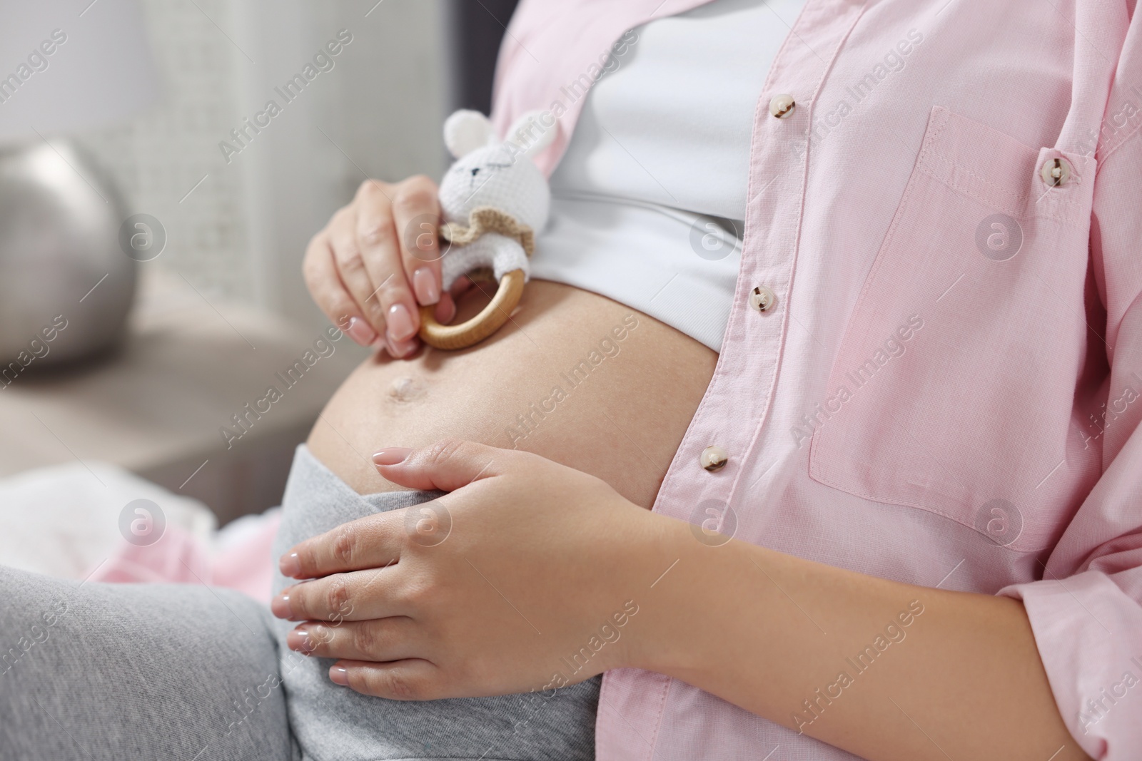 Photo of Pregnant woman with bunny toy lying on bed indoors, closeup