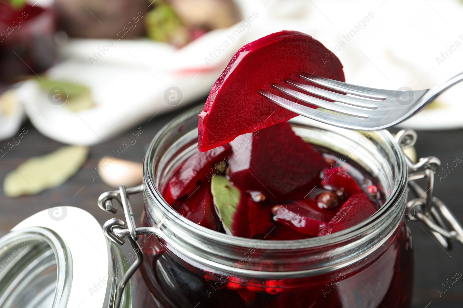 Photo of Fork with pickled beet over glass jar on wooden table, closeup