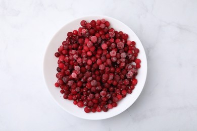 Frozen red cranberries in bowl on white marble table, top view