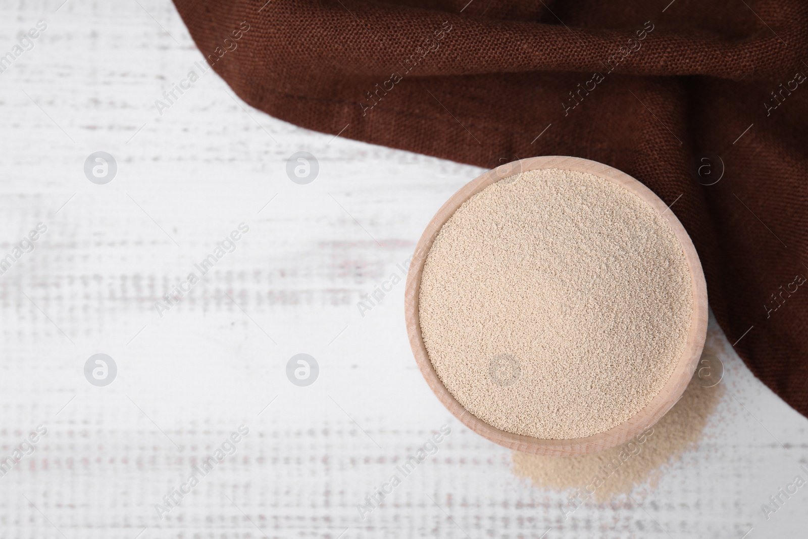 Photo of Granulated yeast in bowl on white wooden table, top view. Space for text