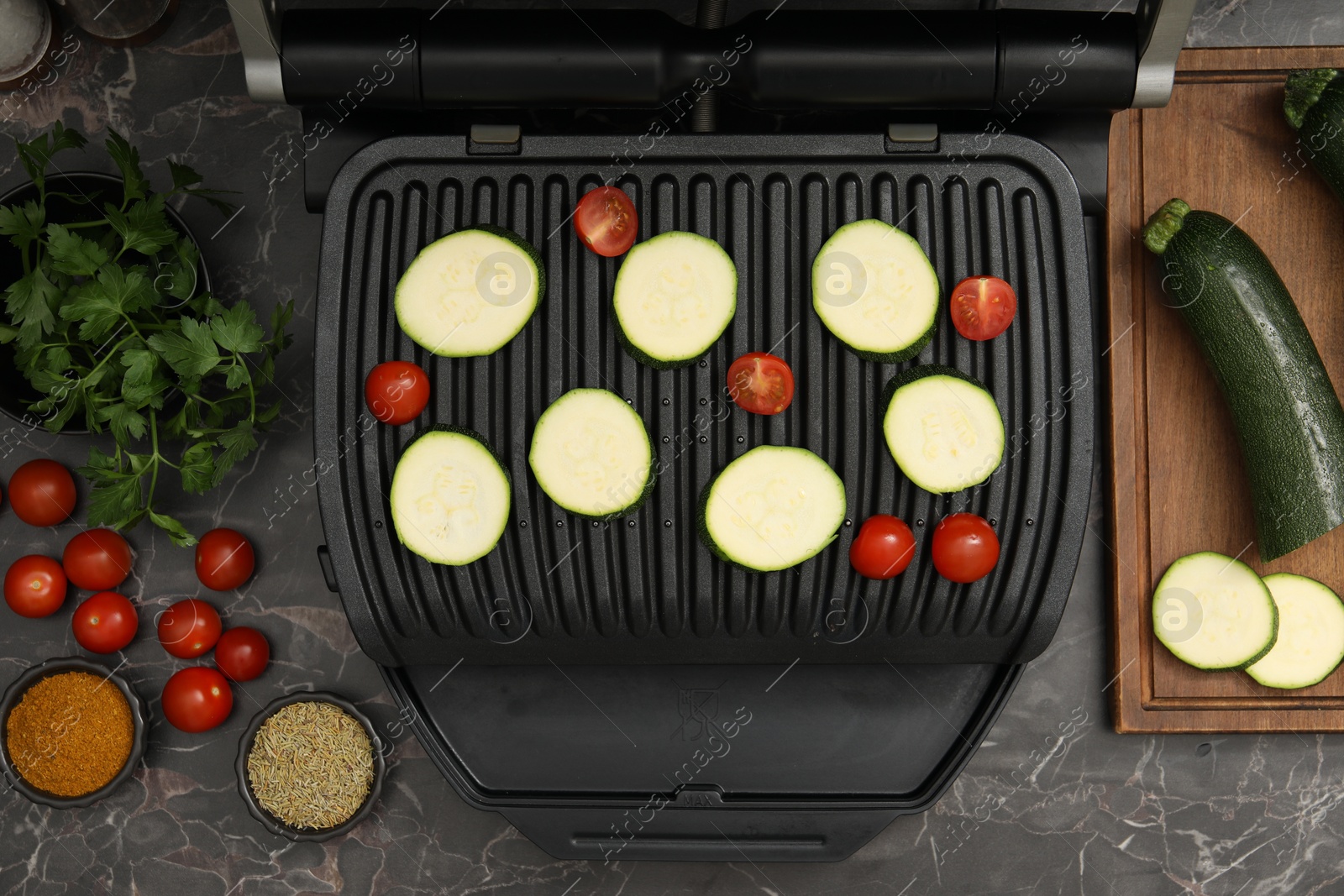 Photo of Electric grill with vegetables and spices on black marble table, flat lay