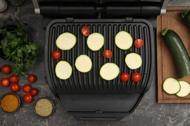 Photo of Electric grill with vegetables and spices on black marble table, flat lay