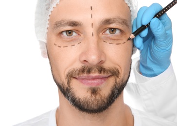 Doctor marking mature man face before cosmetic surgery on white background