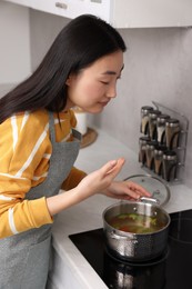 Photo of Beautiful woman cooking and smelling soup in kitchen