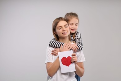 Photo of Little daughter congratulating her mom with postcard on white background, space for text. Happy Mother's Day