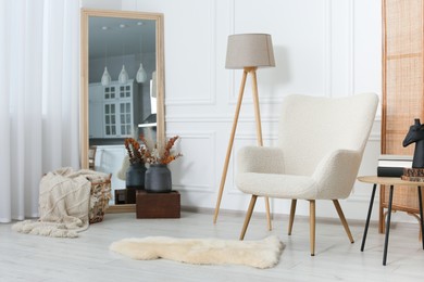 Stylish beige armchair, small coffee table and mirror in living room. Interior design