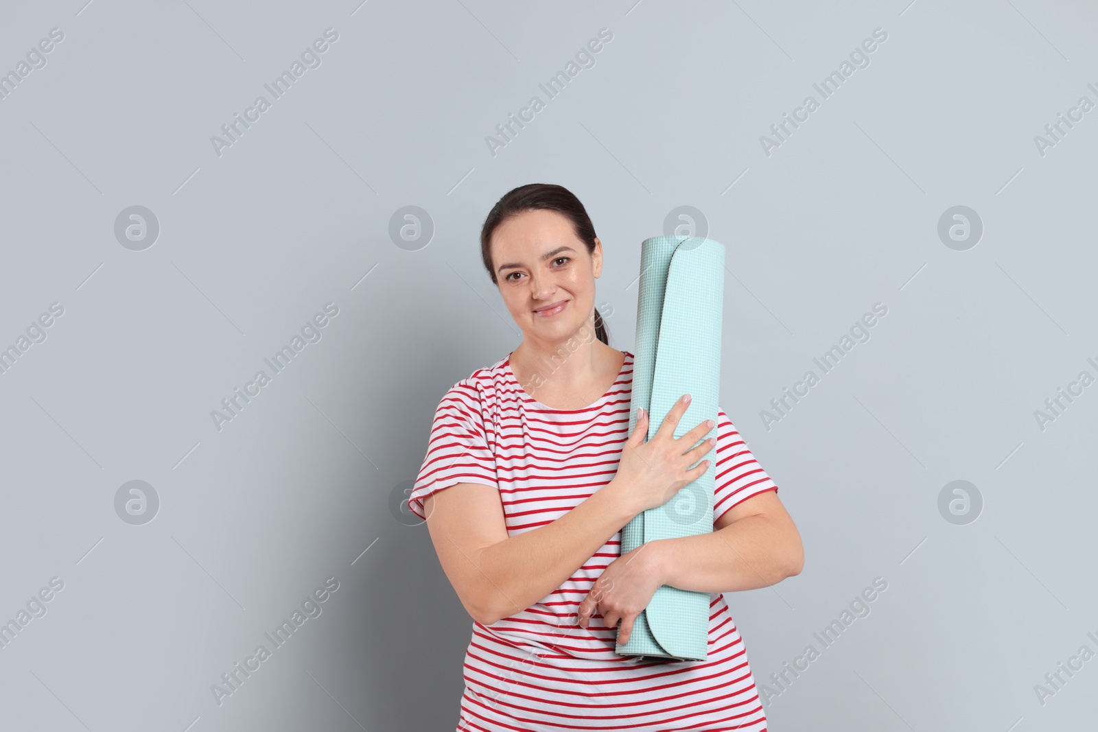 Photo of Happy overweight woman with yoga mat on grey background