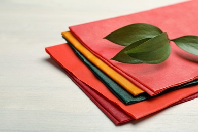 Photo of Colorful beeswax food wraps and fresh leaves on white wooden table, closeup