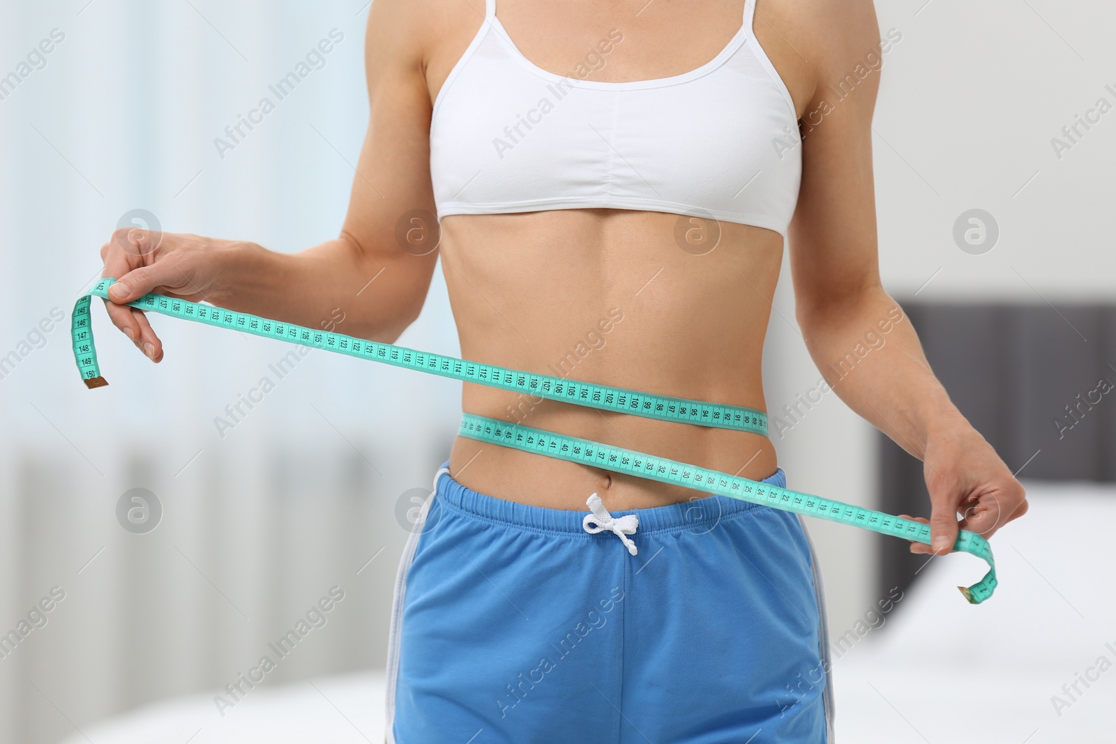 Photo of Slim woman measuring waist with tape at home, closeup. Weight loss