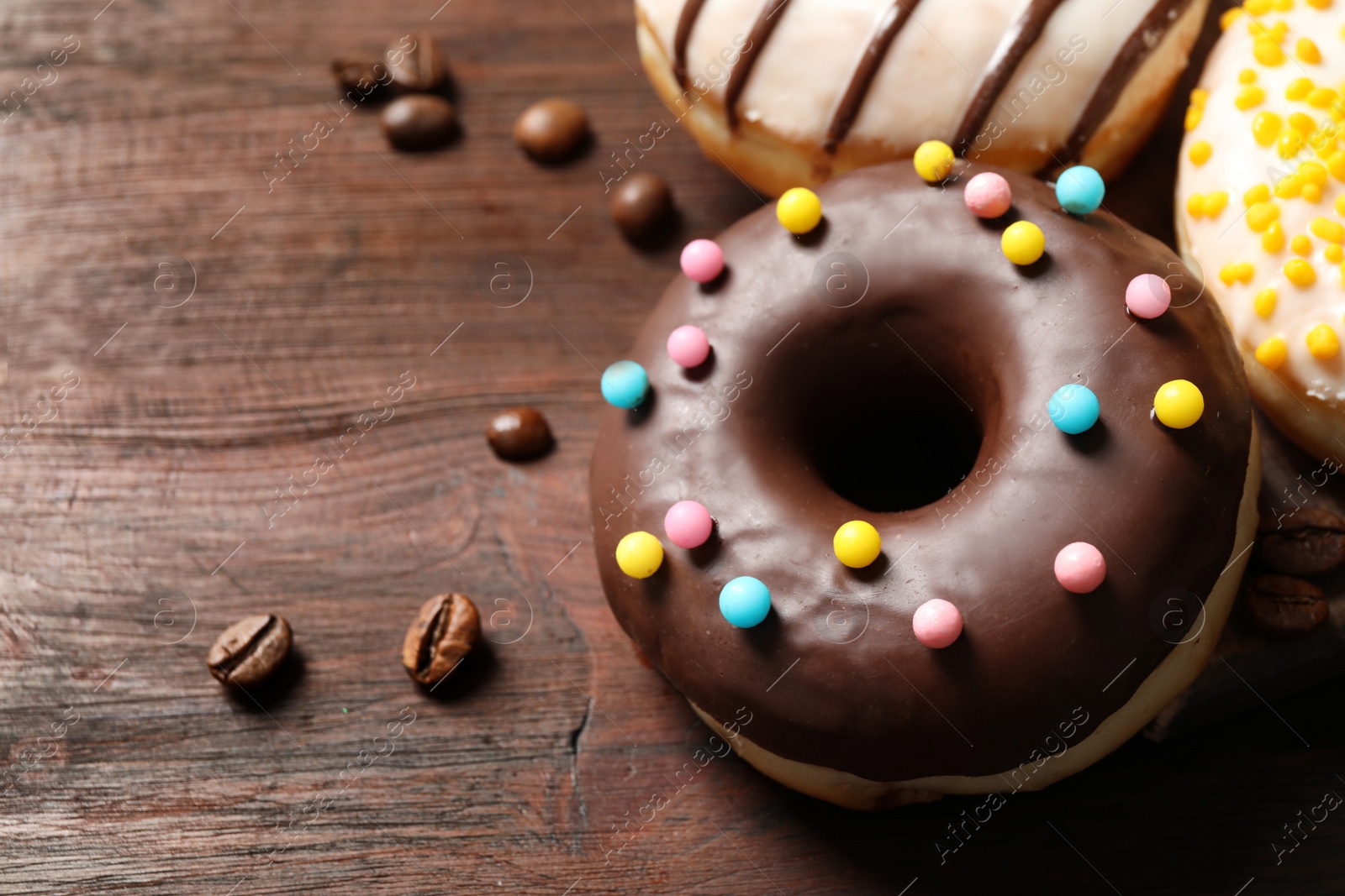 Photo of Yummy donuts with colorful sprinkles on wooden table, closeup. Space for text