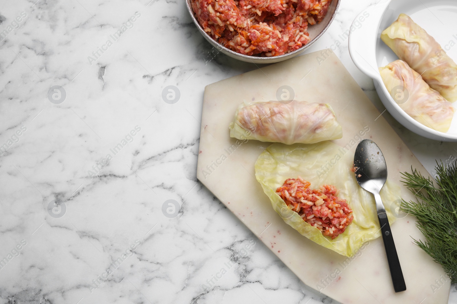 Photo of Preparing stuffed cabbage rolls on white marble table, flat lay. Space for text