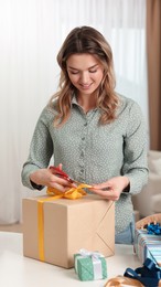 Photo of Beautiful young woman wrapping gift at table indoors